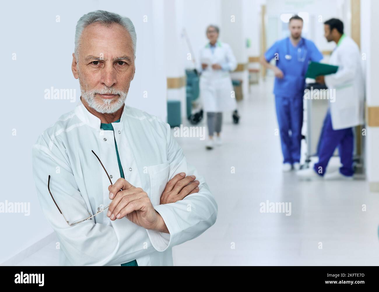 Experienced male general practitioner wearing medical uniform standing with arms crossed in modern medical clinic while working day, portrait Stock Photo