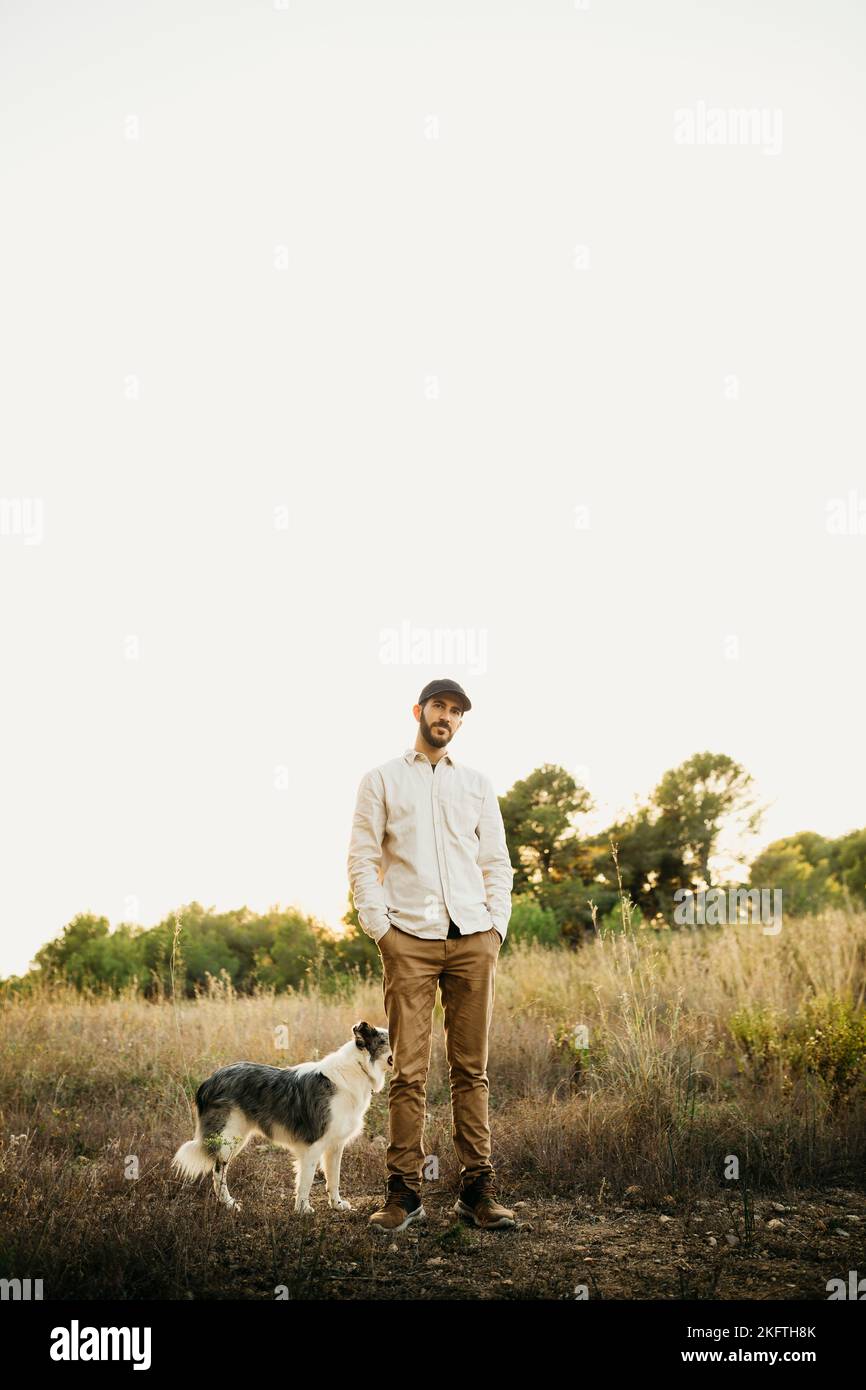 Portrait of a young bearded man wearing a black cap, with his dog, at countryside Stock Photo