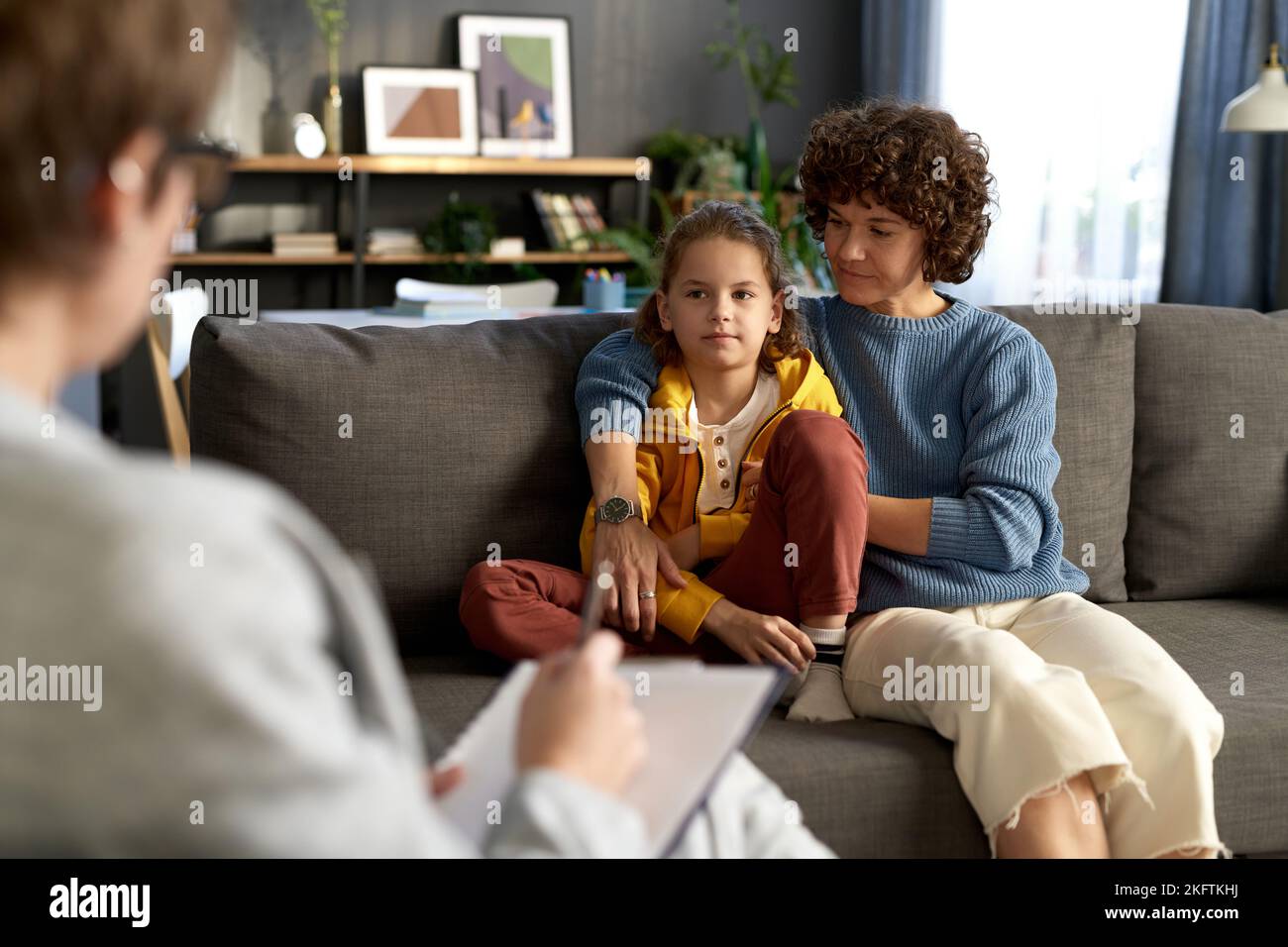 Mother sitting on sofa together with her son in living room and talking to child psychologist Stock Photo