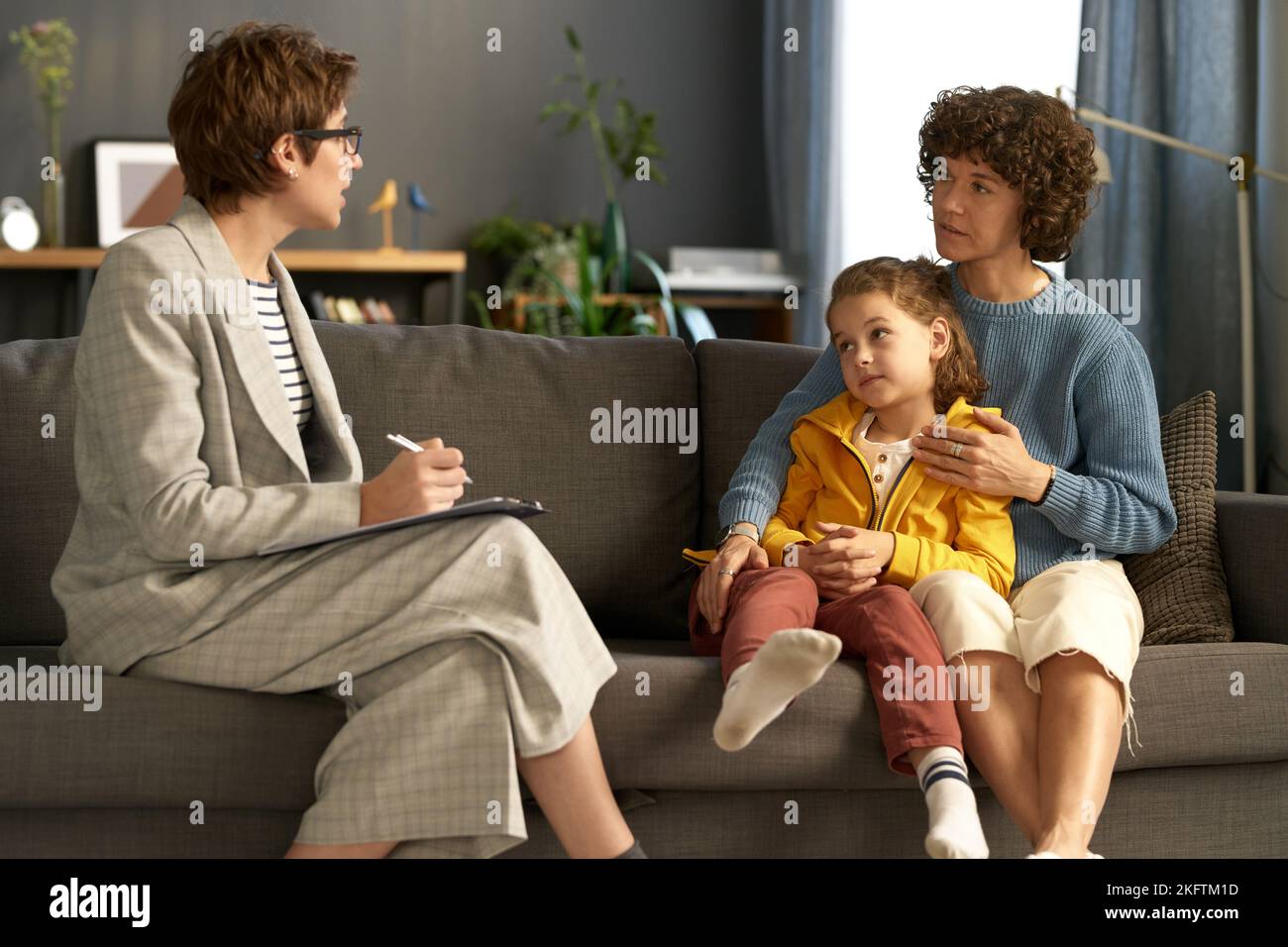 Social worker making notes while talking to adoptive parent and child during their meeting at home Stock Photo