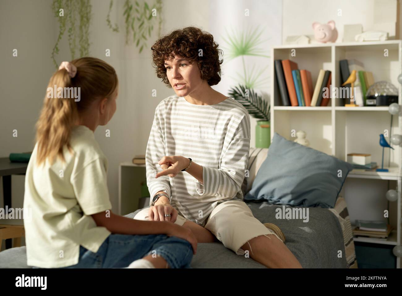 Mother having serious conversation with her daughter, she talking about her bad behavior while they sitting in bedroom Stock Photo
