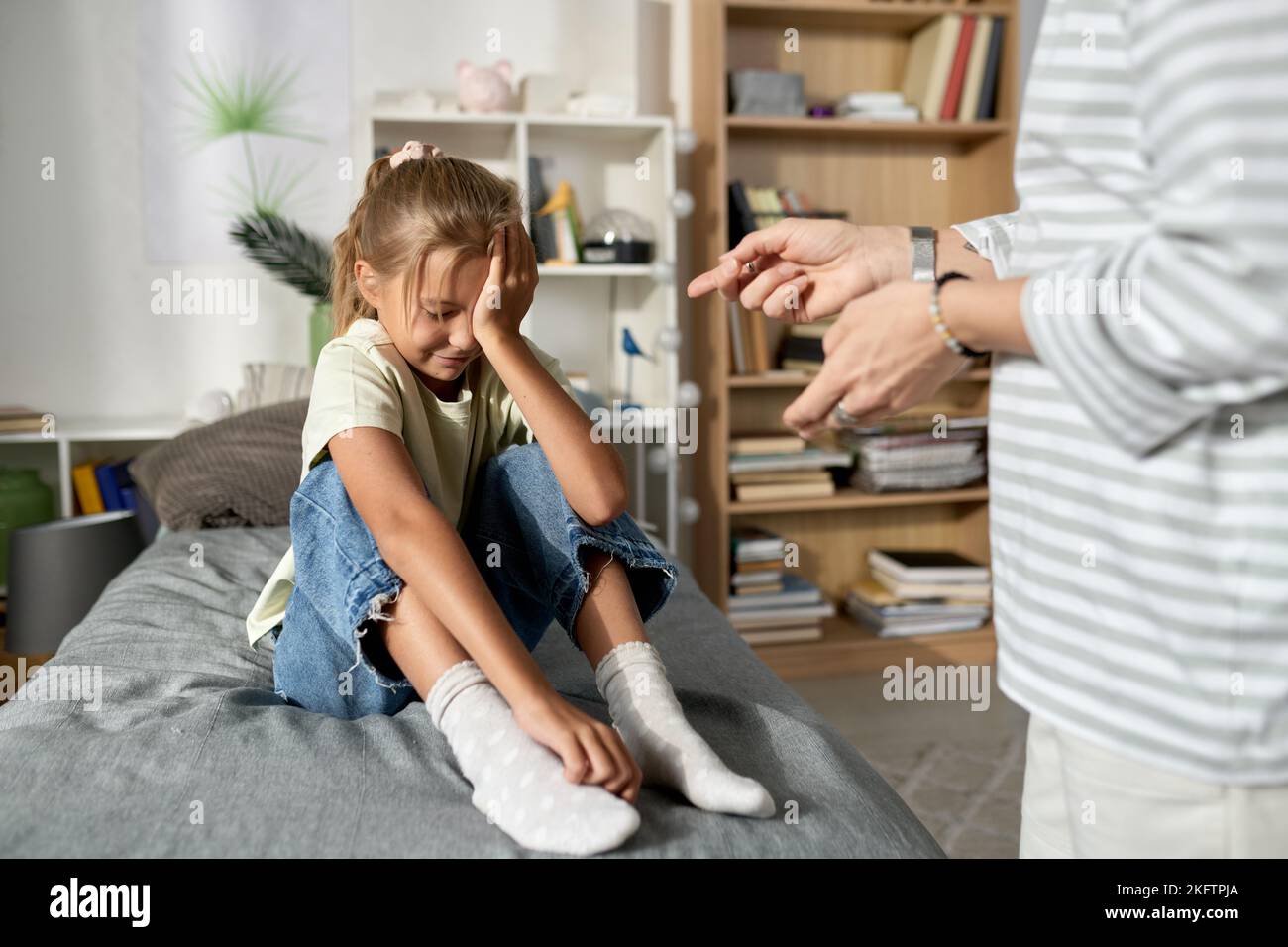 Little girl sitting on her bed and crying while her mom scolding her for bad behavior Stock Photo