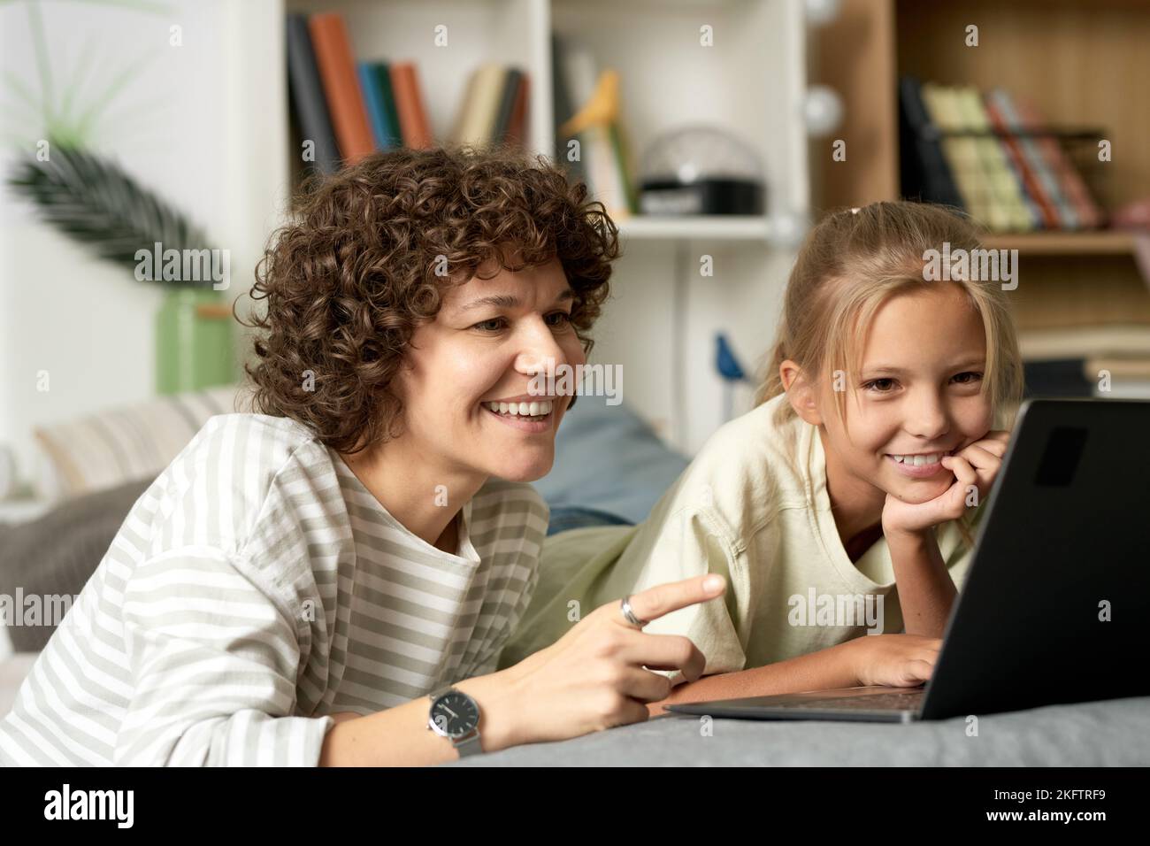 Happy mother watching funny video on laptop together with her daughter, they looking at monitor and laughing Stock Photo