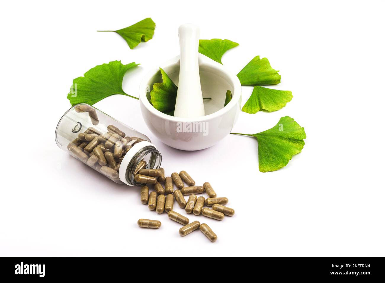 Pills and fresh green ginkgo biloba leaves, mortar and pestle on white background. Top view. Stock Photo
