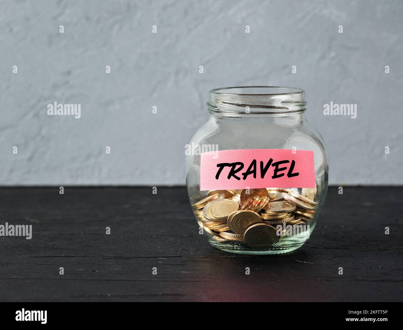 Glass jar with coins and the word travel on a label. Saving money for holiday travel and budget for vacation. Stock Photo
