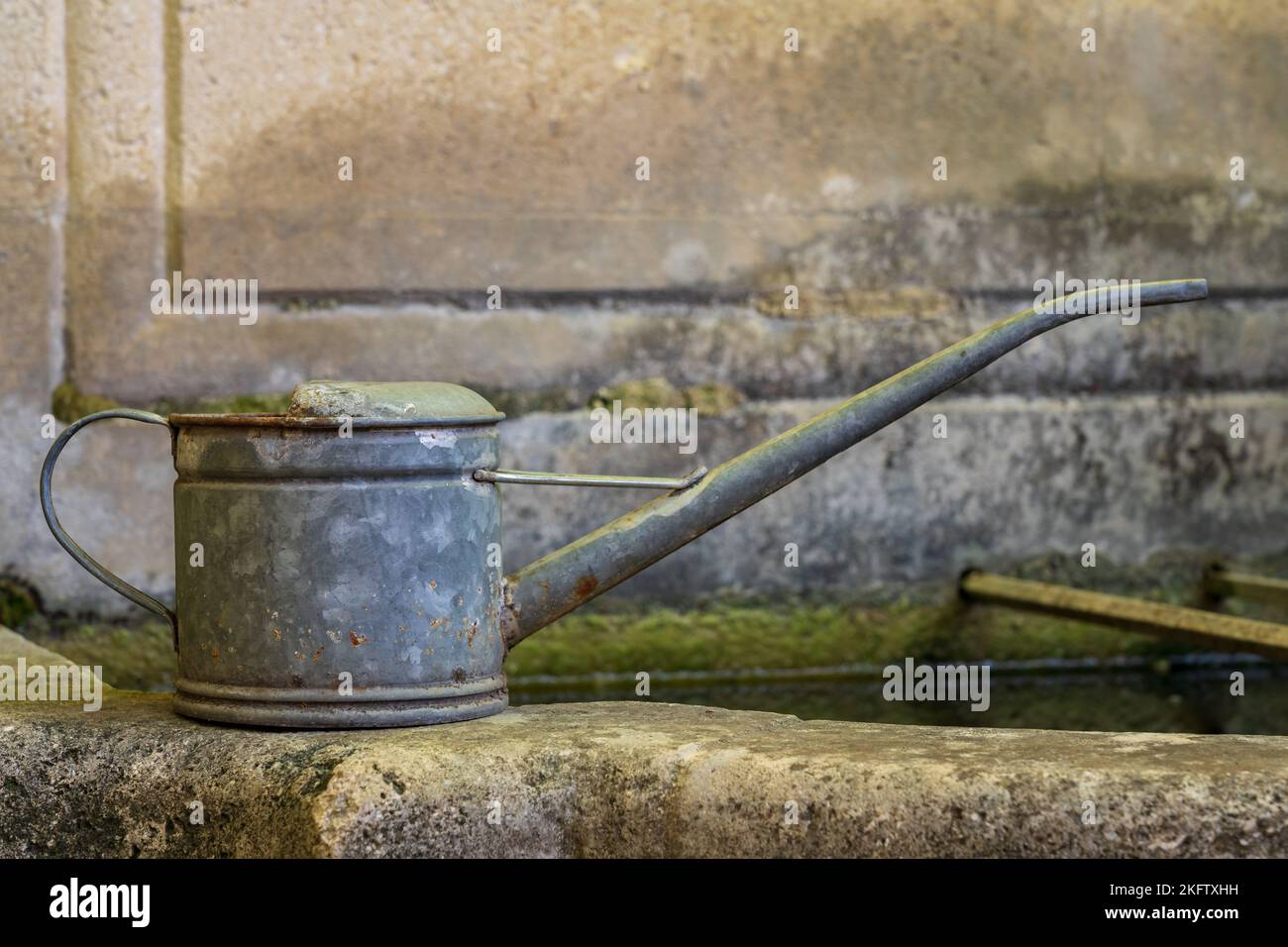 Closeup profile view of traditional vintage tin watering can isolated on stone fountain edge in garden Stock Photo