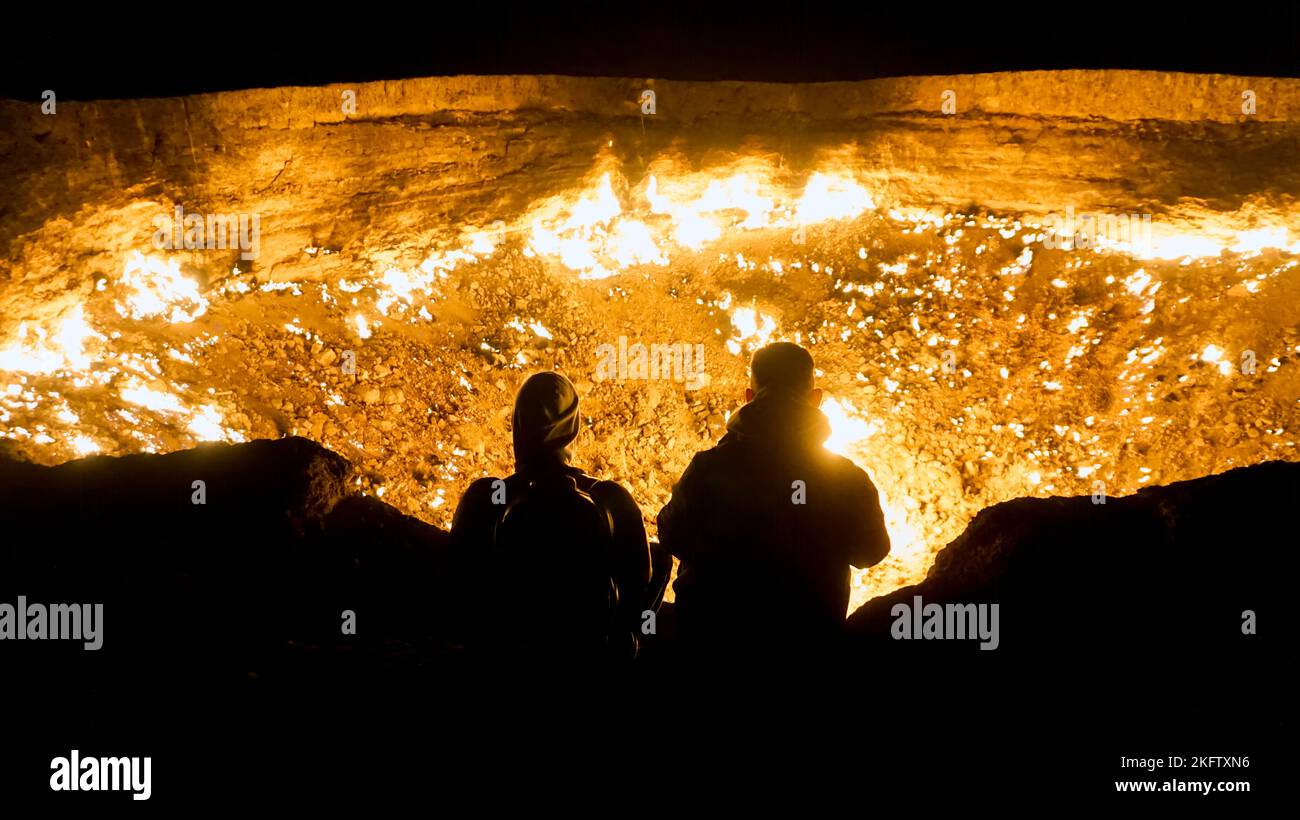 Two persons at the edge of the flaming gas crater in Darwaza, Turkmenistan, also known as The Doors of Hell or The Gates of Hell. Stock Photo