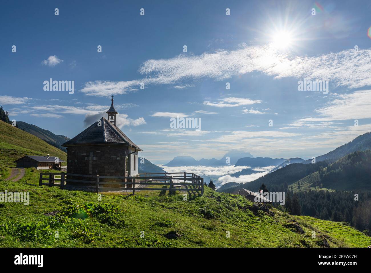The chapel on the Ackernalm in front of the Kaiser mountains in the backlight of the morning sun, Tyrol, Austria Stock Photo