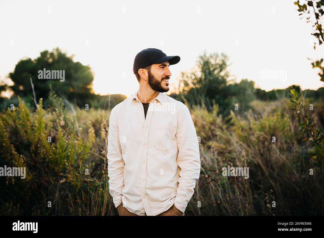 Portrait of a young bearded man wearing a black cap at countryside ...