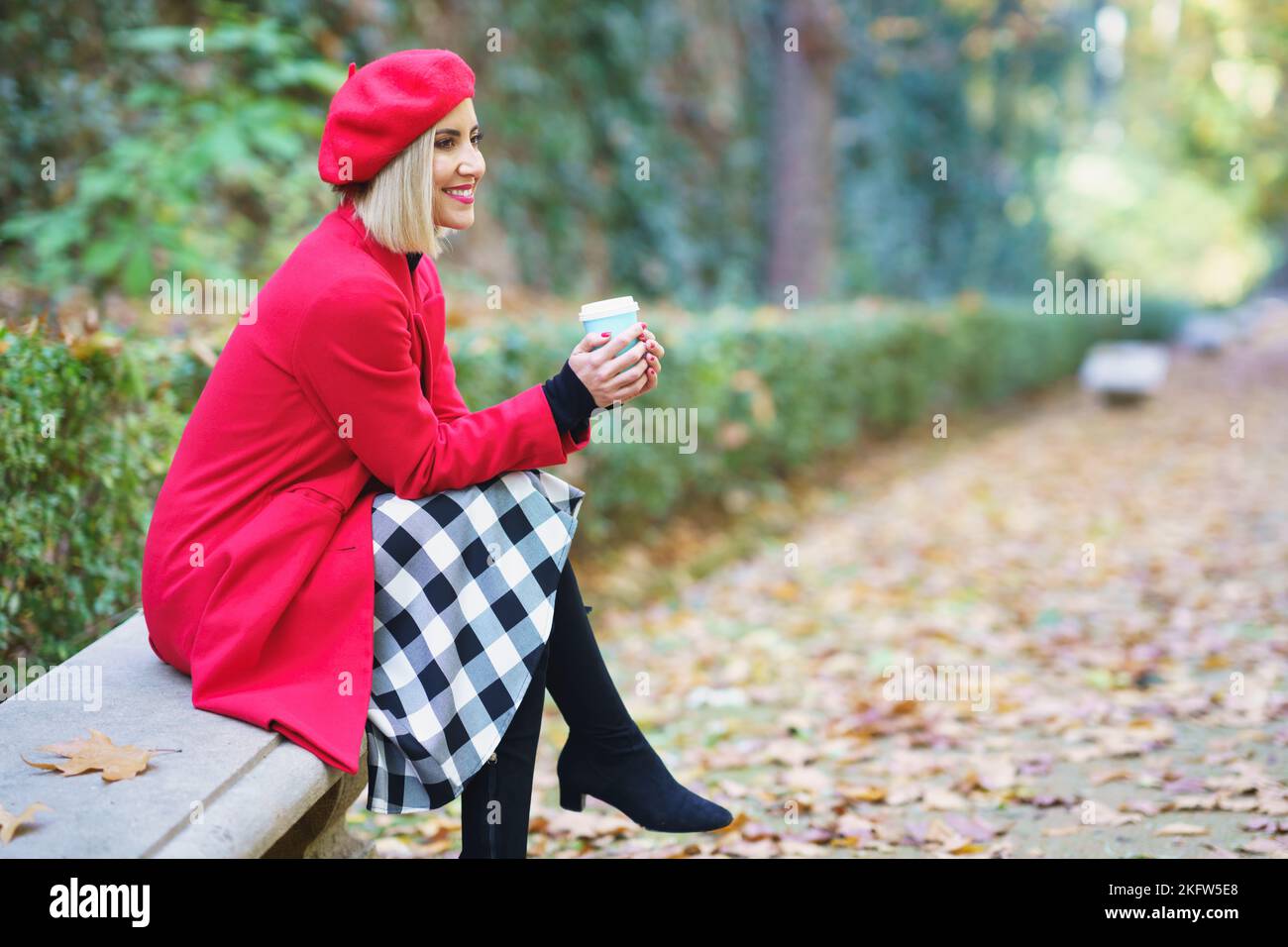 Smiling woman with takeaway drink sitting in park Stock Photo
