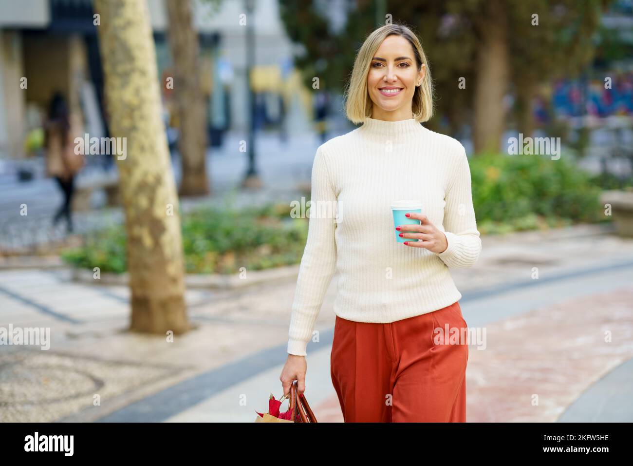 Smiling woman with cup of beverage carrying paper bag Stock Photo