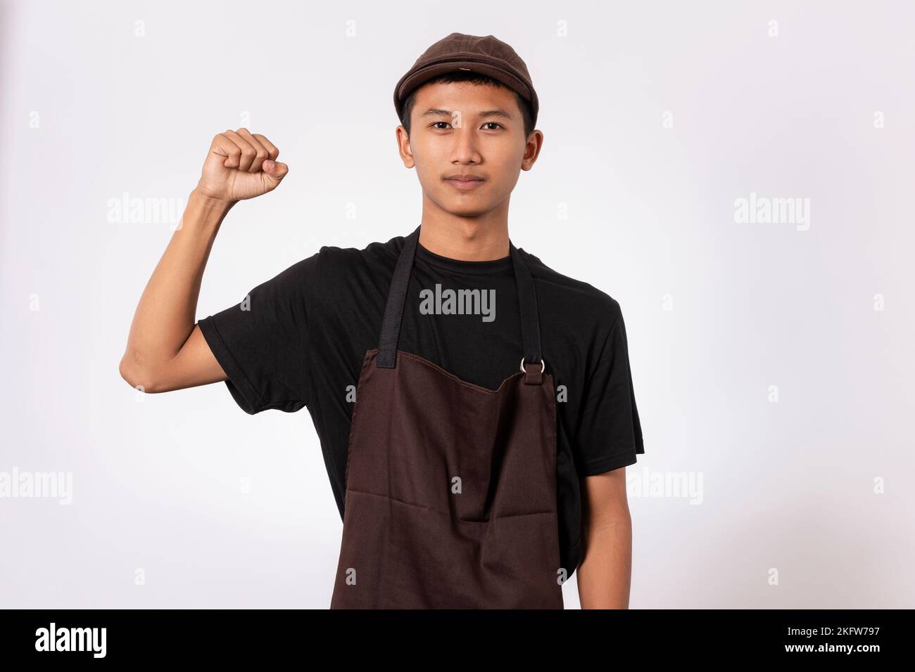 Handsome barista asian man wearing brown apron and black t-shirt isolated over white background very happy and excited celebrating winner with arms ra Stock Photo
