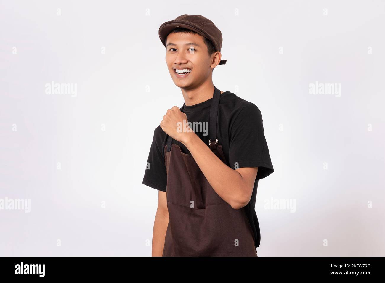 Handsome barista asian man wearing brown apron and black t-shirt isolated over white background very happy and excited celebrating winner with arms ra Stock Photo