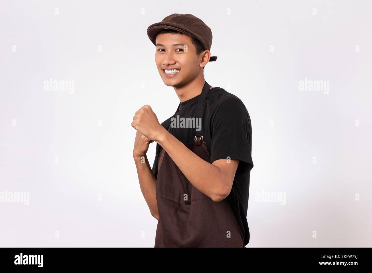 Handsome barista asian man wearing brown apron and black t-shirt isolated over white background very happy and excited celebrating winner with arms ra Stock Photo
