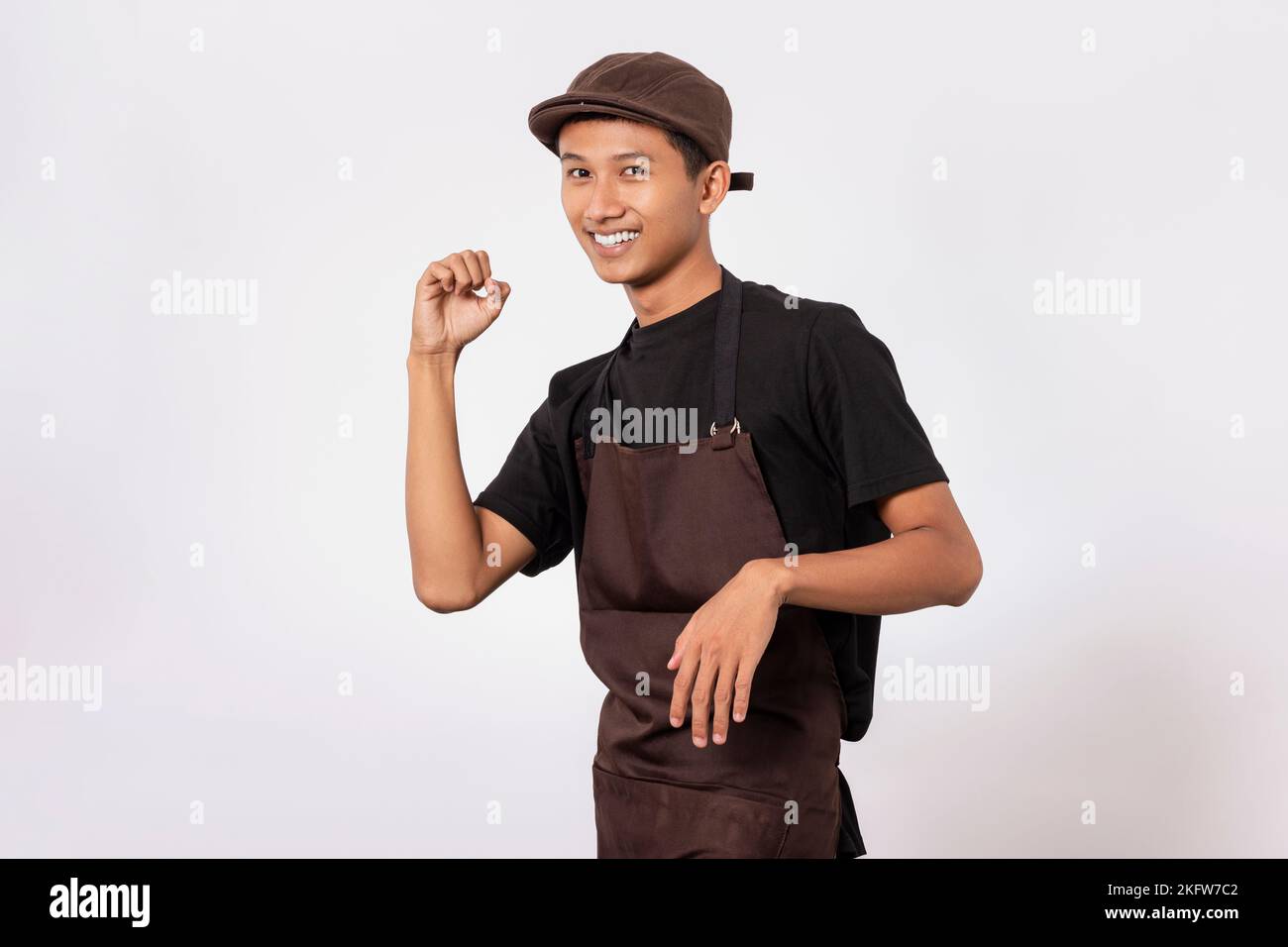 Handsome barista asian man wearing brown apron and black t-shirt isolated over white background very happy and excited celebrating winner with arms ra Stock Photo