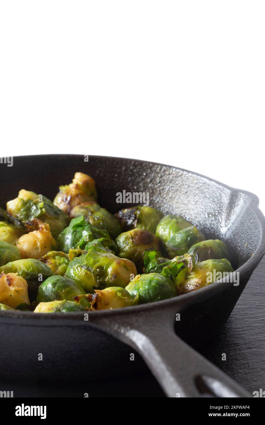 Sprouts fried, in a cast iron frying pan wiyth olive oil, on a slate board. Isolated on a white background Stock Photo
