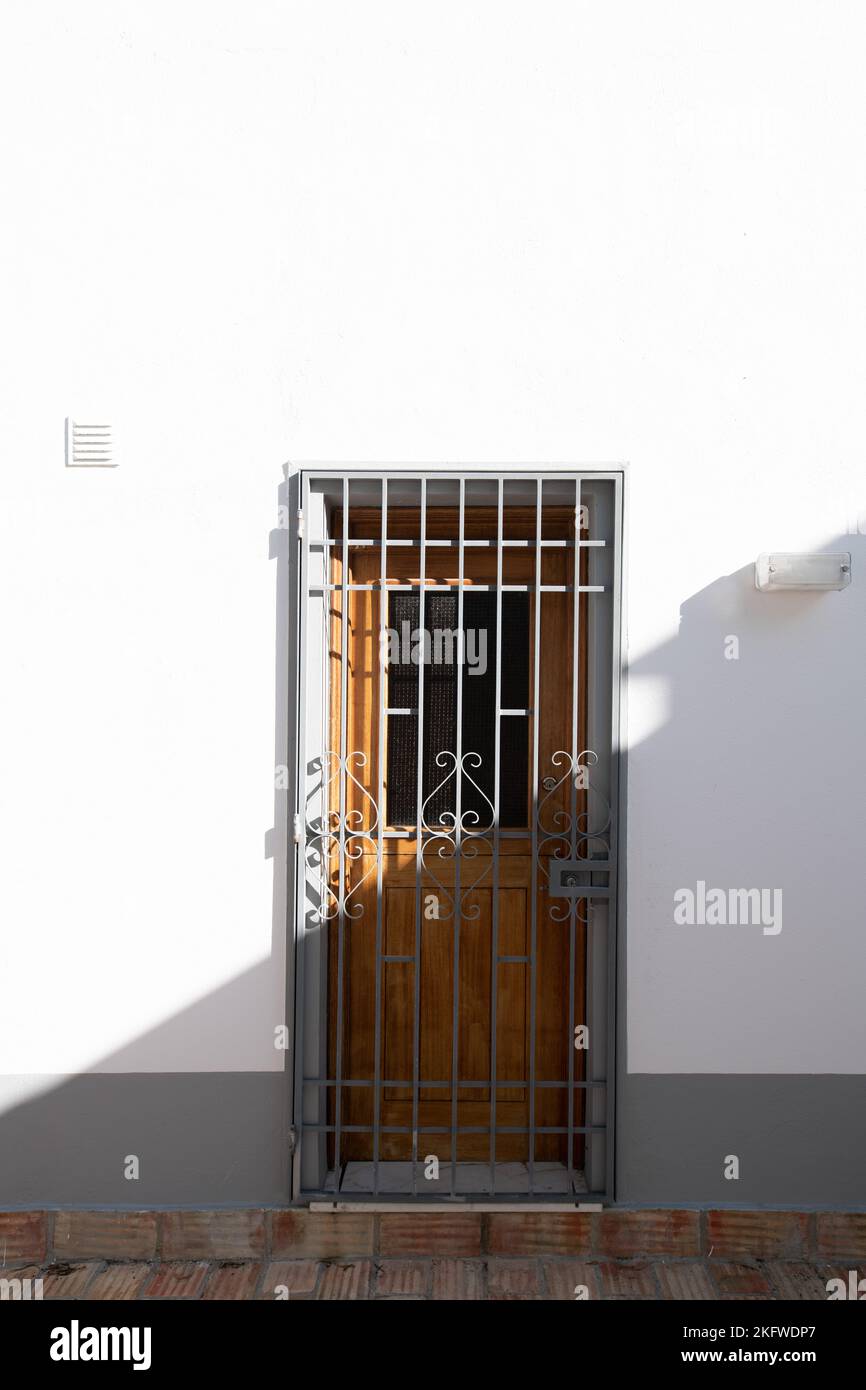 Old fashioned wooden door with a metal security grill half in bright sunlight half in shade Stock Photo