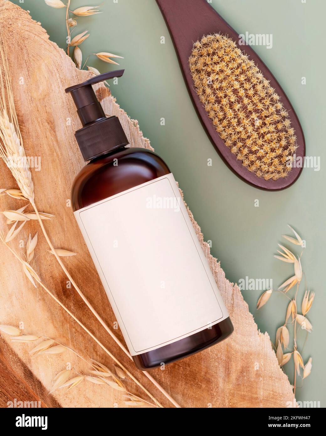 Natural beauty product. Dispenser bottle with beauty product and body wash brush on a wooden podium on a green background with rye and wheat ears. Moc Stock Photo