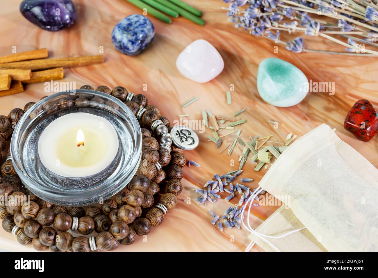 Self-care, healing composition with rosary beads, aroma sticks, chakra stones, sandalwood sticks and candle on a pink marble podium. Concept of relaxi Stock Photo