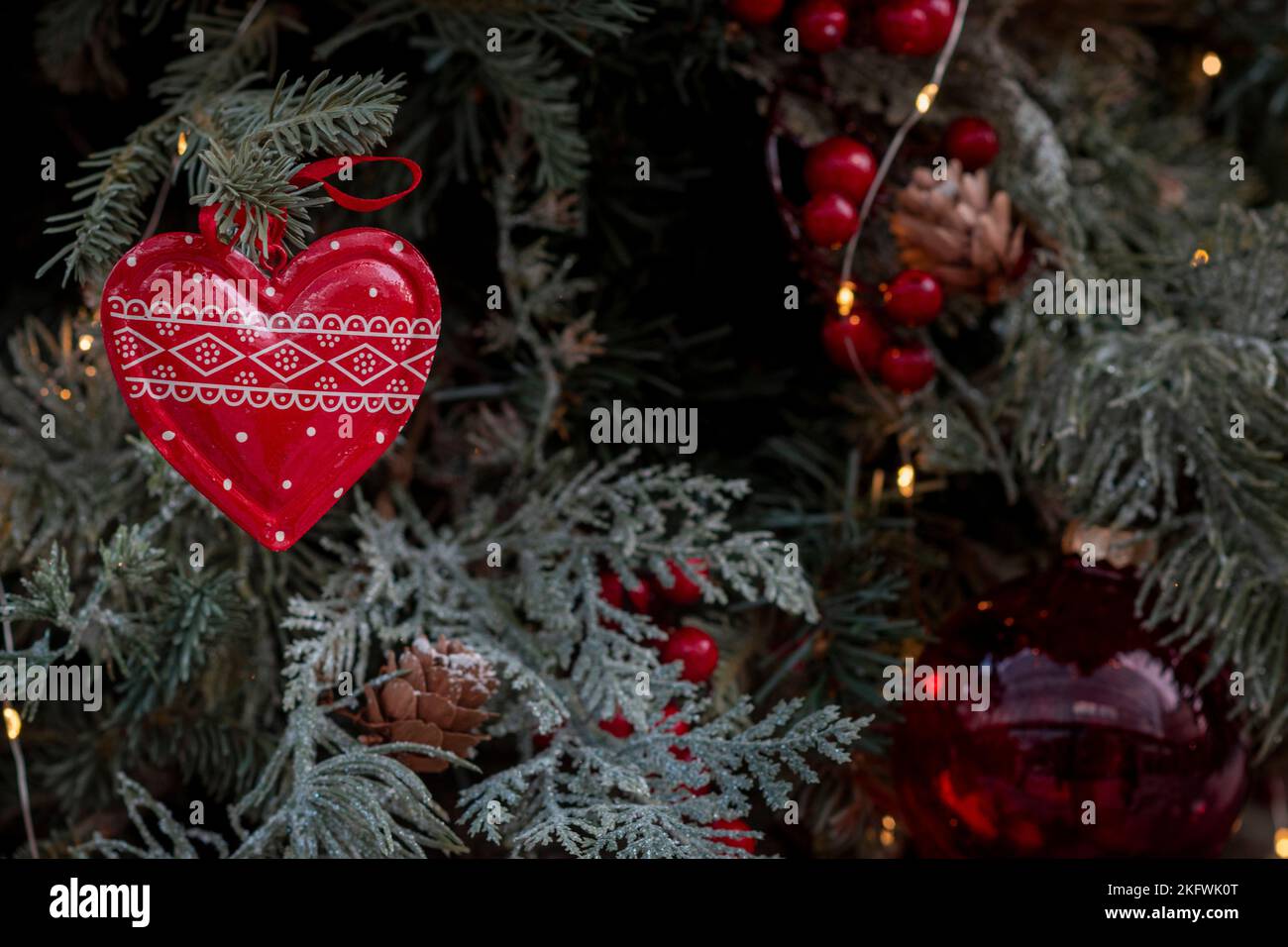 Traditional carved heart shaped Christmas ornament closeup hanging on the branch of a Christmas tree with fairy lights in the background Stock Photo