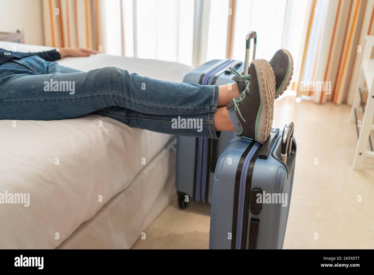 Woman lying on her hotel bed with her feet in her suitcases on arrival at her vacation spot. Stock Photo