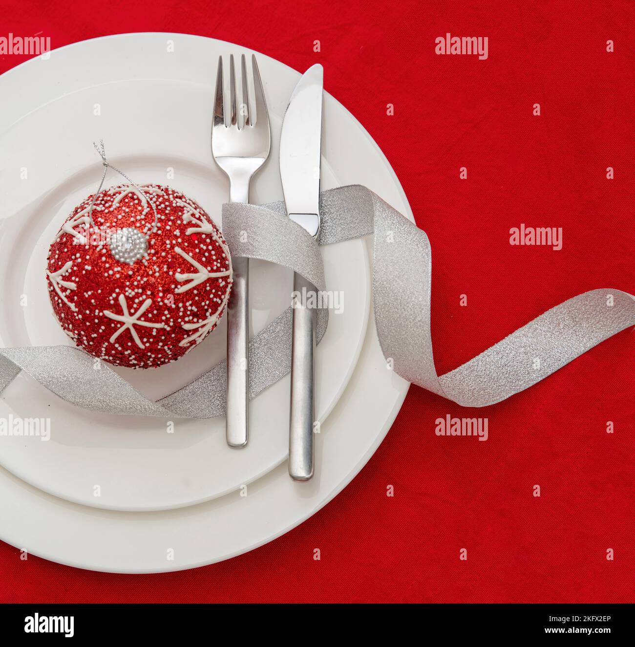Christmas table setting. Xmas bauble and silver cutlery on plates, red background, top view. Holiday celebration dinner Stock Photo