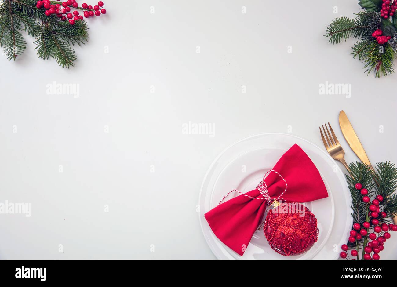 Christmas table setting, celebration dinner flat lay. Golden Cutlery, red cloth napkin and Xmas decoration on white background, top view, copy space Stock Photo