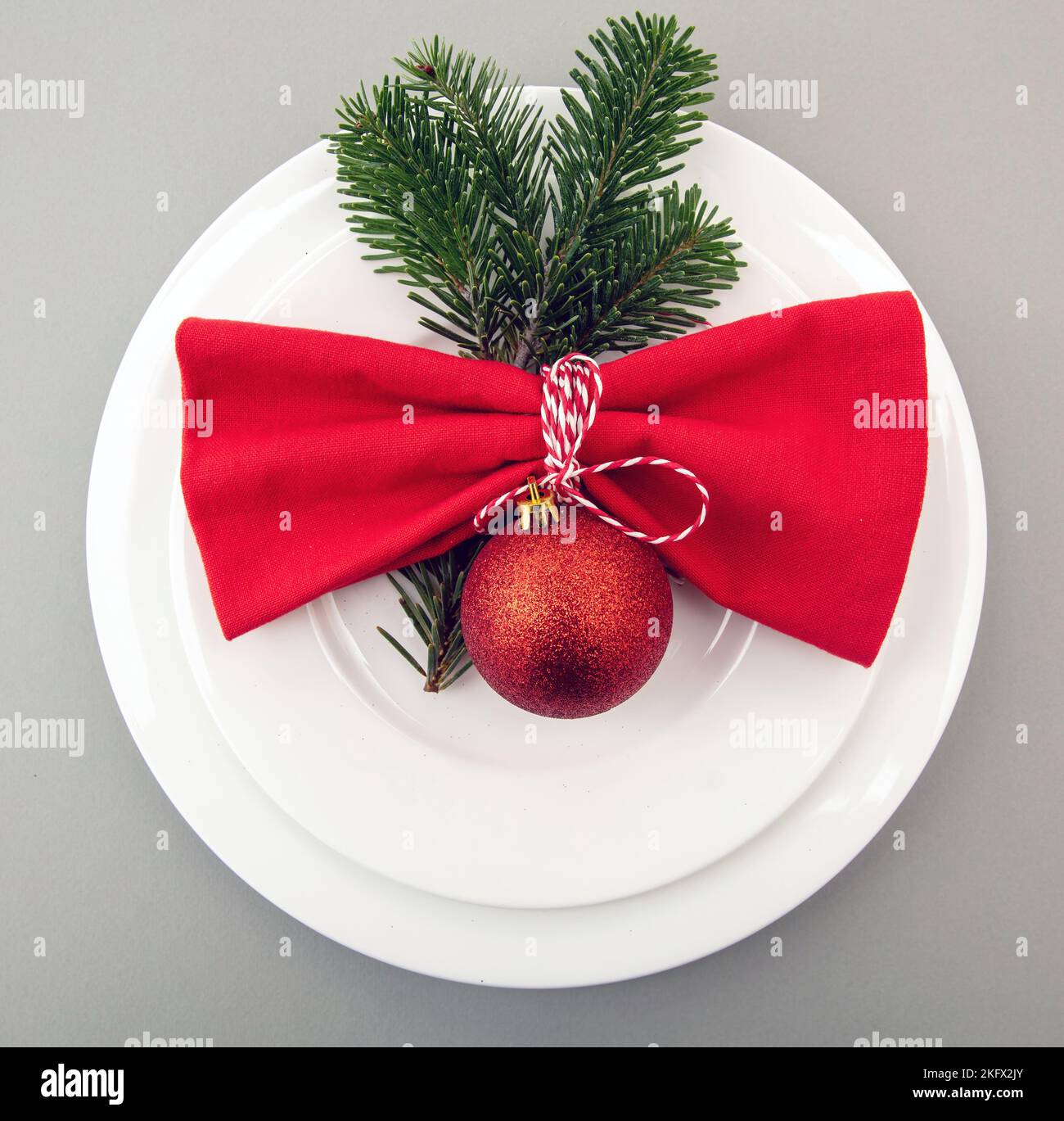 Christmas table setting, celebration dinner. Red cloth napkin and Xmas decoration on white plates set, gray background, top view Stock Photo