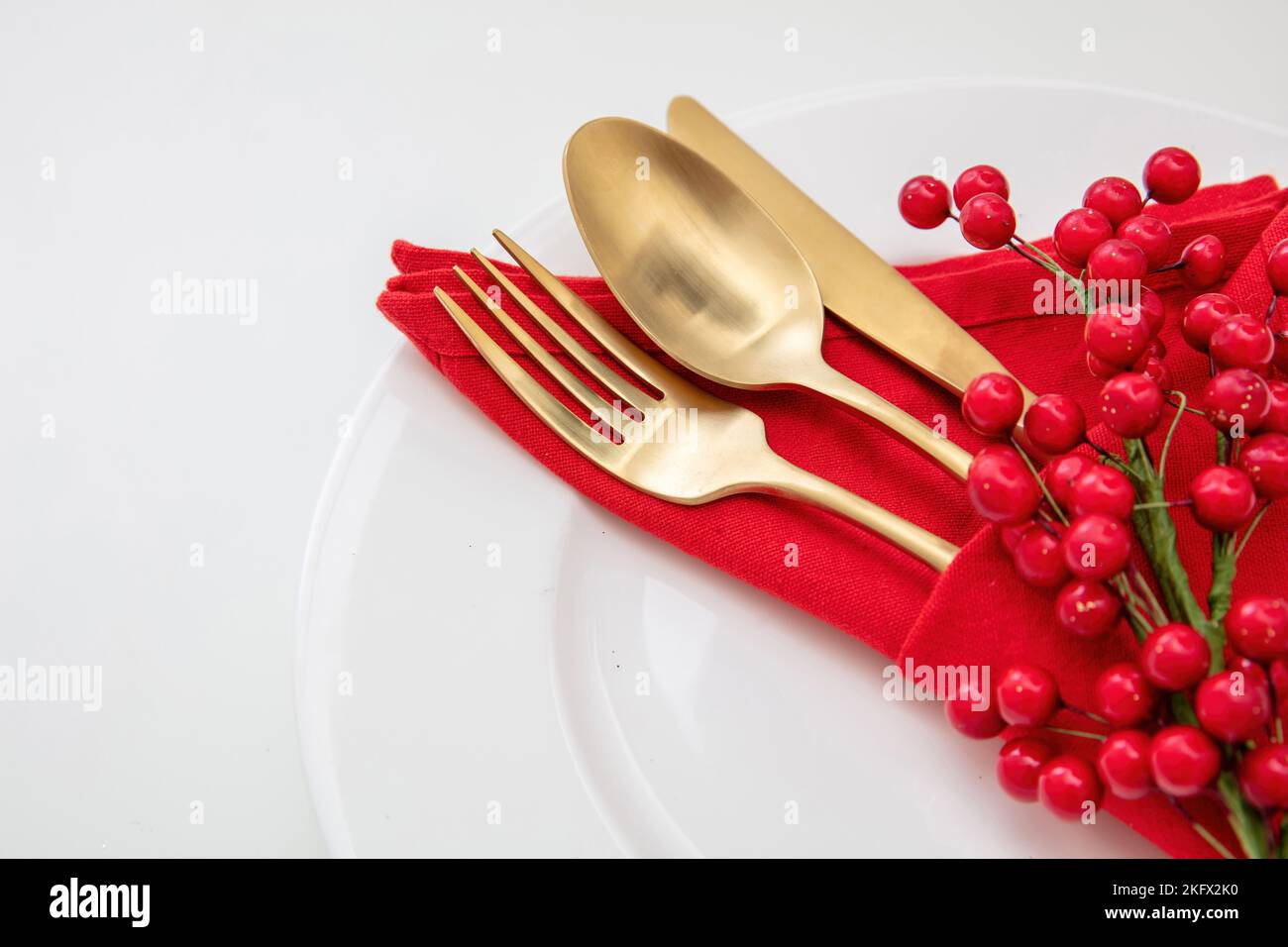 Holiday table setting. Golden Cutlery and red cloth napkin on white plate, close up view. Christmas New Year celebration dinner Stock Photo