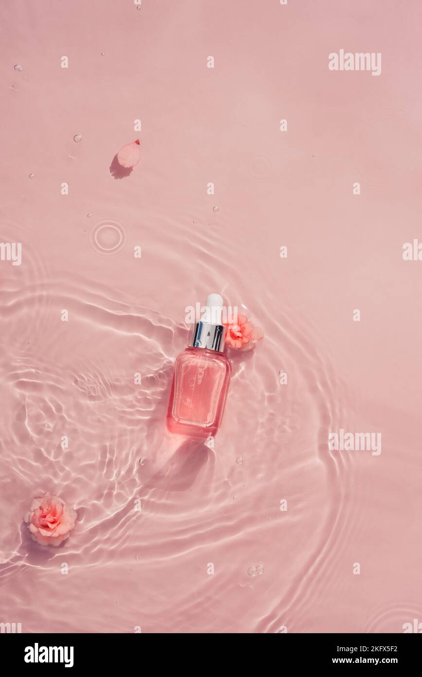 Cosmetic bottle with serum, collagen, oil in water wave and pink roses. Moisturizing skin care cosmetic concept Stock Photo
