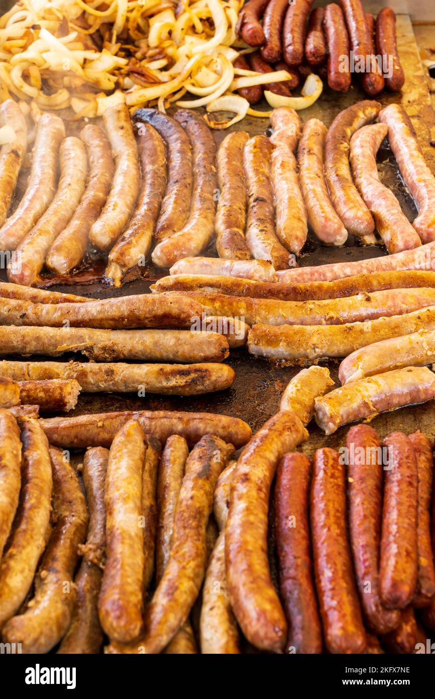 Food. Close up view of long thin sausages and some onions cooking on a hot plate during a open air event Stock Photo