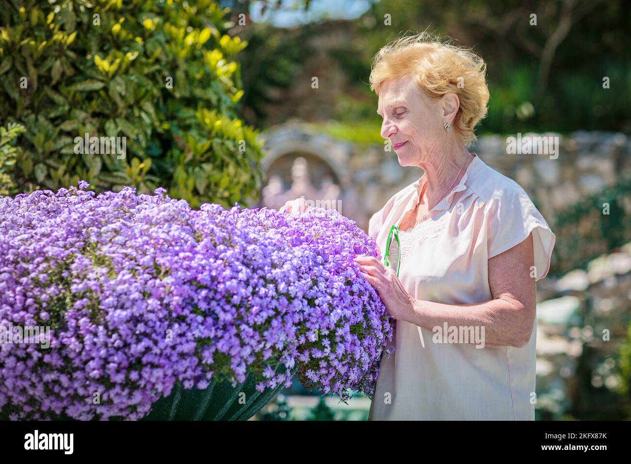 Elderly woman standing near a large flower pot with purple flowers ...
