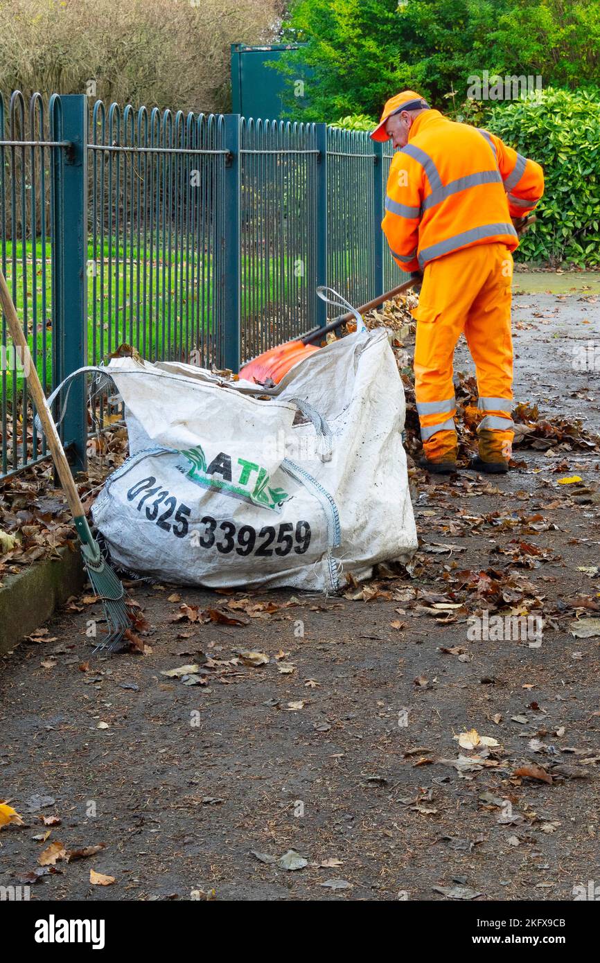 Park keeper sweeping fallen leaves on an autumn day in Locke Park Lake Redcar North Yorkshire Stock Photo