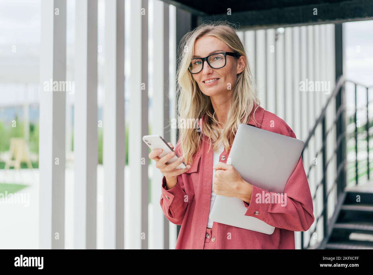 Happy blond business woman in pink jacket holding laptop computer Stock ...