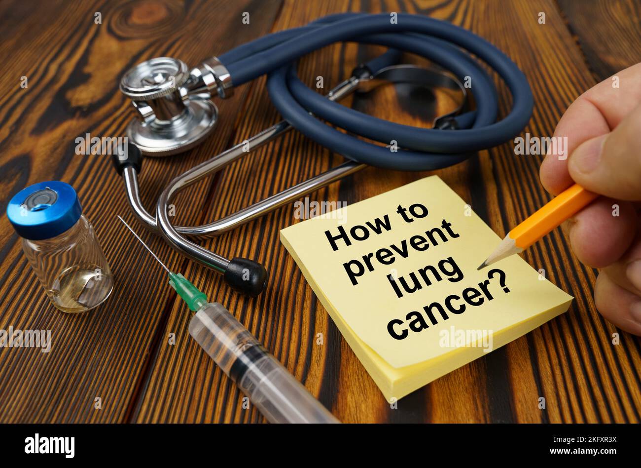Medical concept. On the table is a stethoscope, a syringe, a man's hand with a pen makes an inscription on a sticker - How to Prevent Lung Cancer Stock Photo