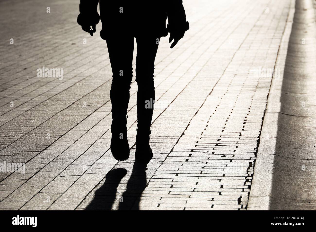 Black silhouette and shadow of lonely slim girl walking on a street. Female legs in tight jeans and boots, dramatic life Stock Photo