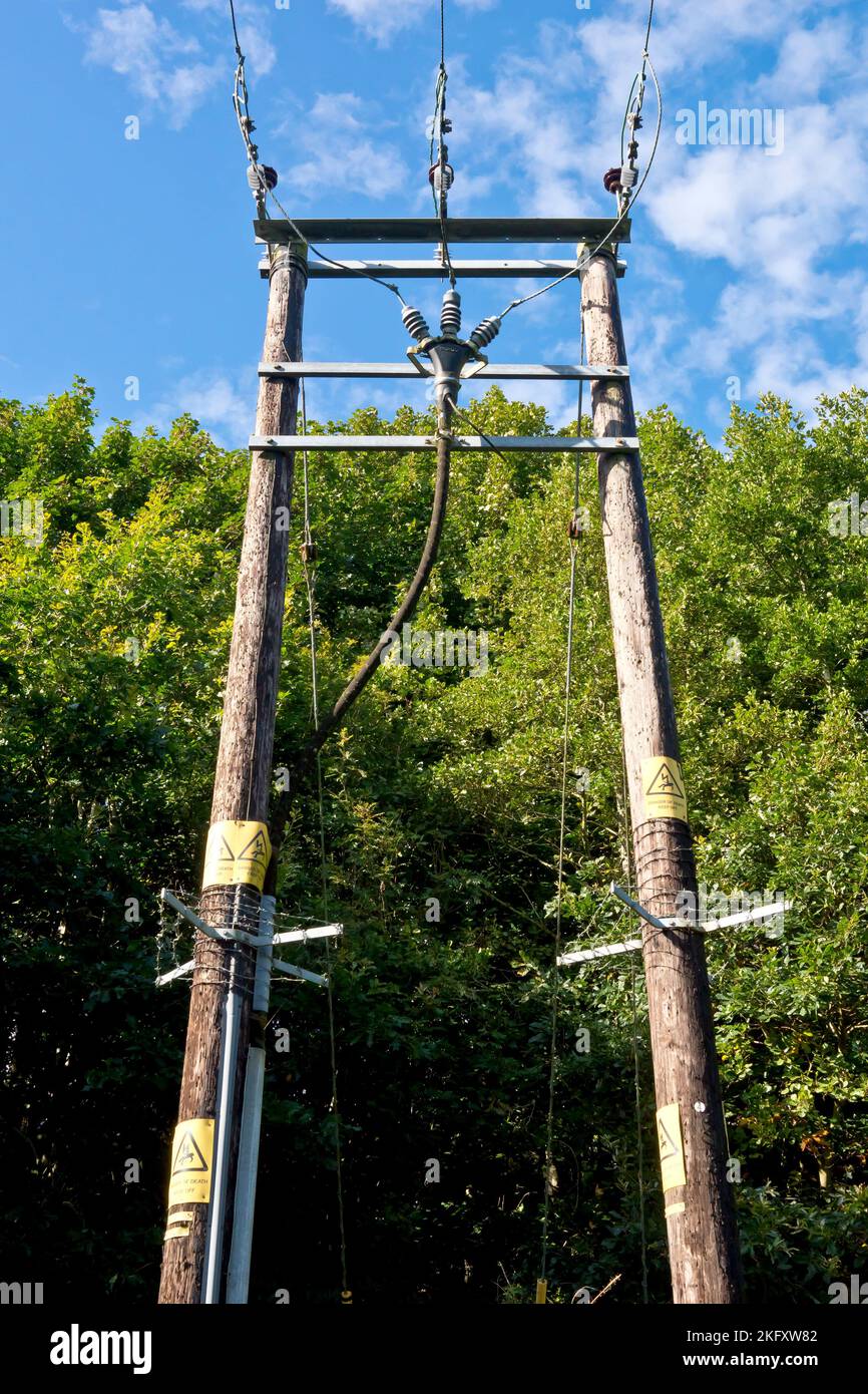 A sturdy rural wooden electricity pylon built to carry three high voltage cables across a river, shot against a blue cloud-flecked sky. Stock Photo