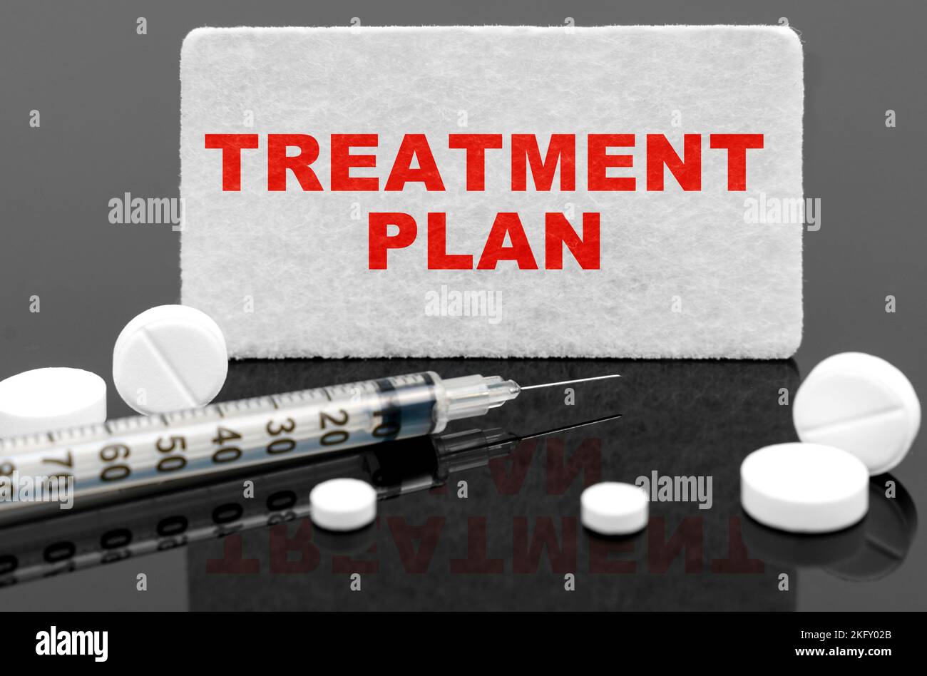 Medicine and health concept. On a black reflective surface, pills, a syringe and a sign with the inscription - TREATMENT PLAN Stock Photo