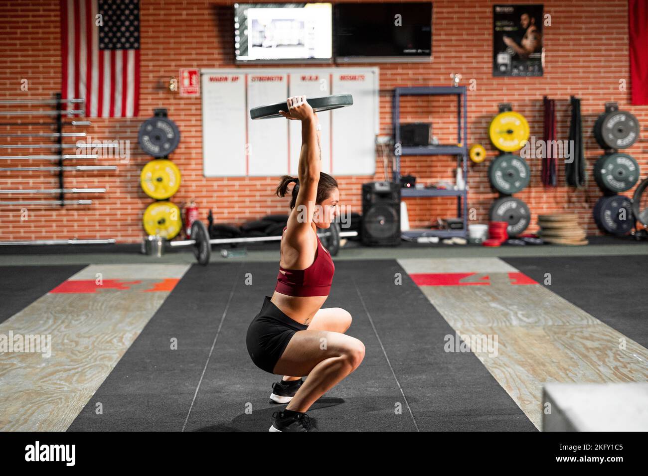 squatting caucasian girl making great effort to hold the big dumbbell