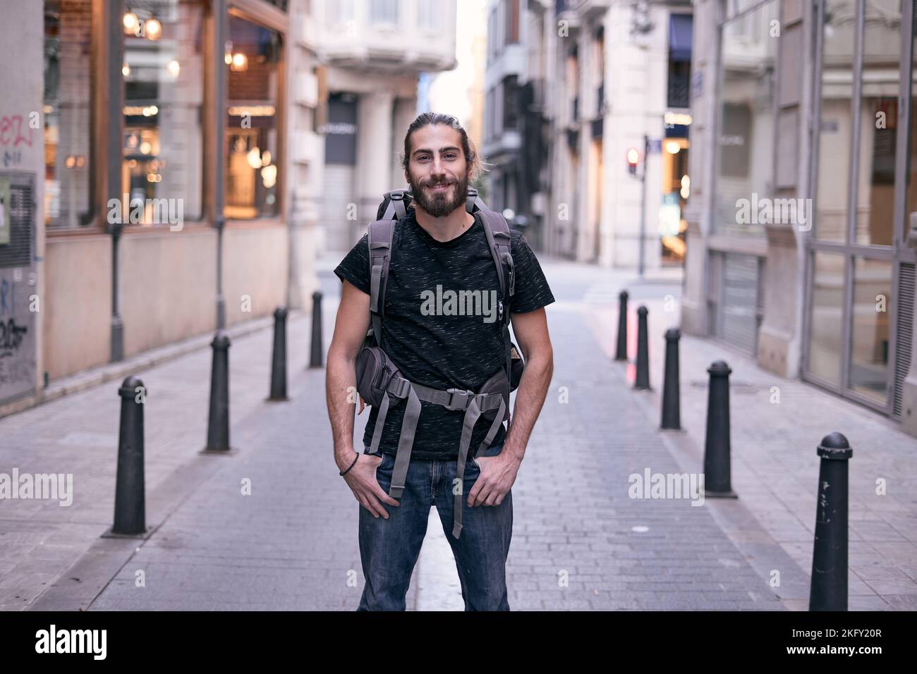 bearded caucasian young man standing on a pedestrian street looking at ...