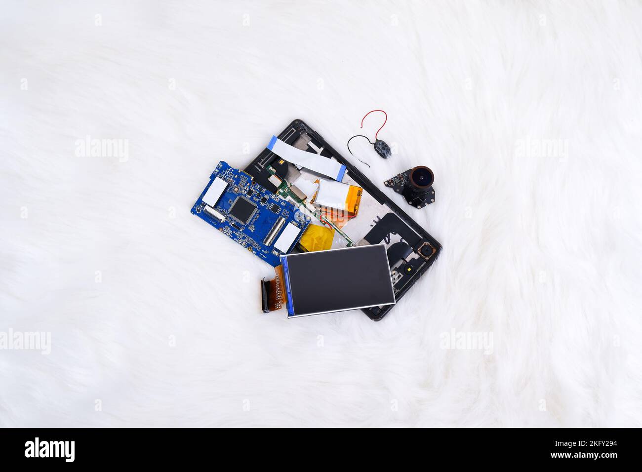 Electronics waste including a lcd screen,a electronic board,a battery,a camera lens and smartphone on white fur rug background Stock Photo