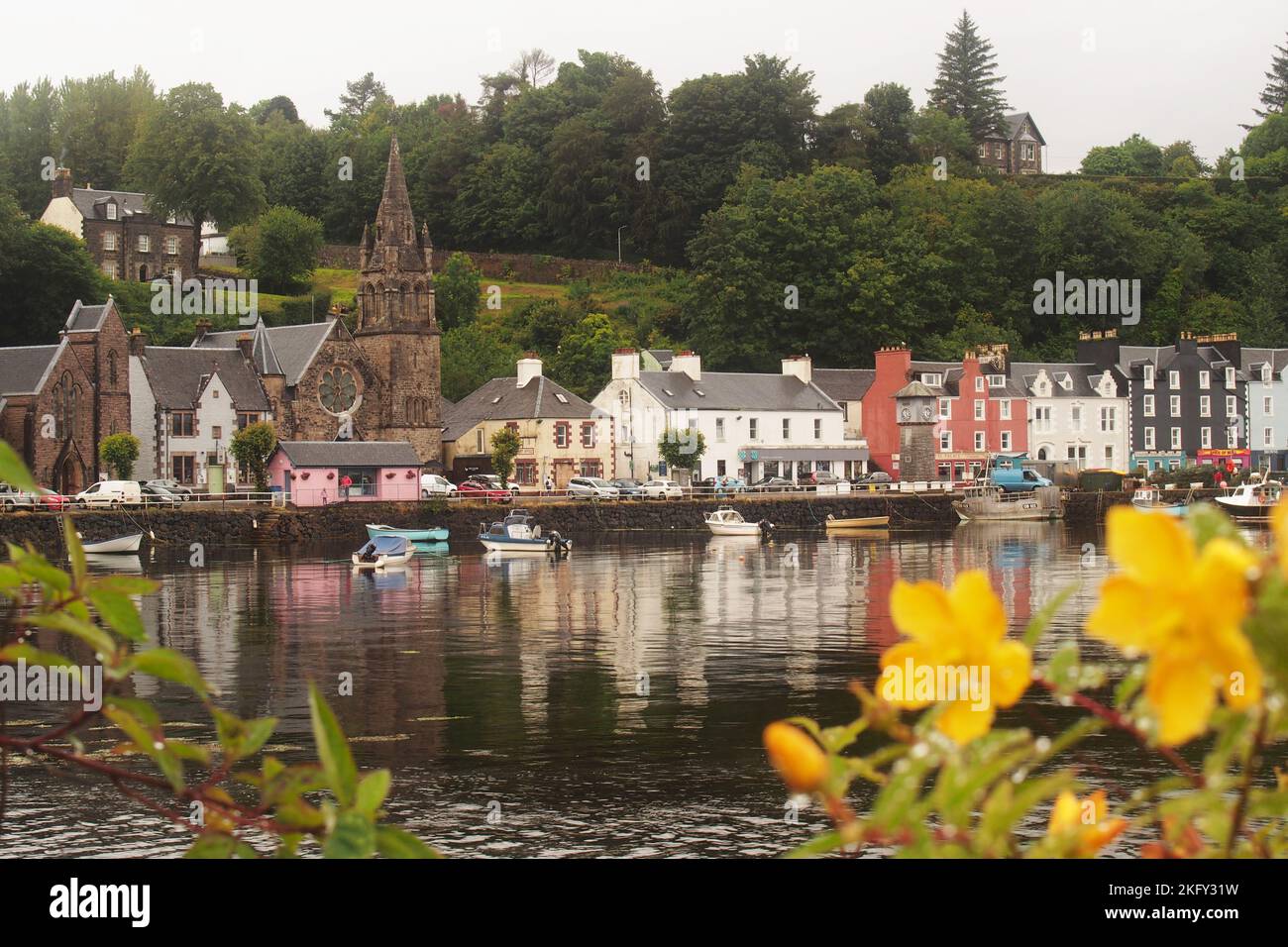 A view across the sea front at Tobermory, Mull, Scotland showing the colourful row of houses along the harbour wall and steep hill behind Stock Photo