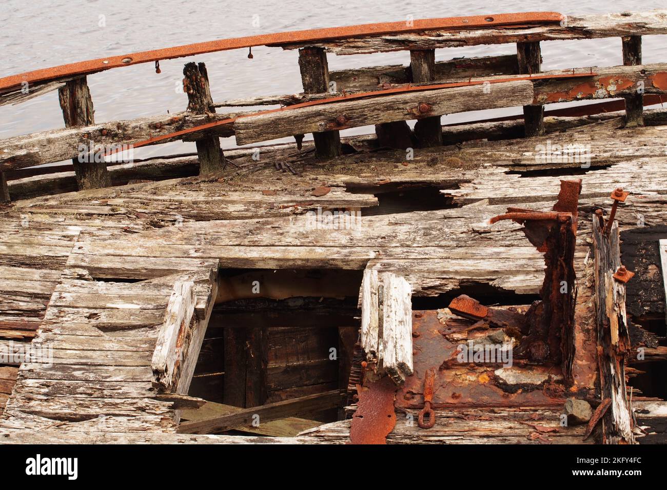An large, old, wrecked wooden boat, in dry dock, showing the rotting timbers, nuts and bolts and