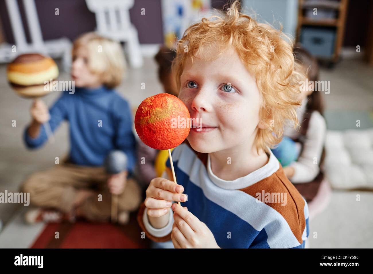 Adorable gingerhaired boy holding model of Mars by his face