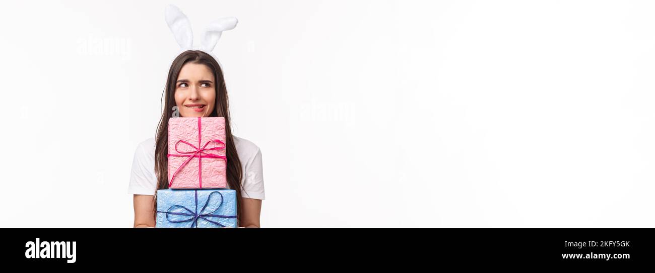 Celebration, holidays and presents concept. Portrait of troubled and doubtful young cute girl in rabbit ears, biting lip and look away, thinking she Stock Photo