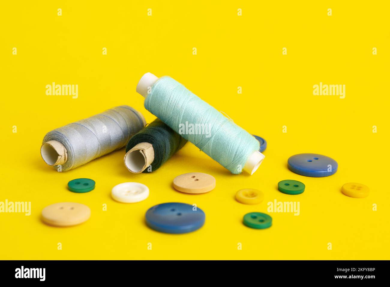 Thread spools and different buttons on yellow background Stock Photo