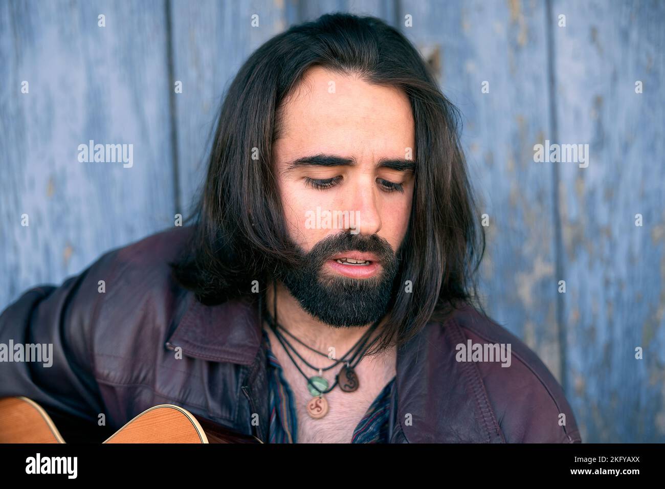 closeup face young caucasian man with fur jacket beard and long hair sitting in the doorway of a house Stock Photo