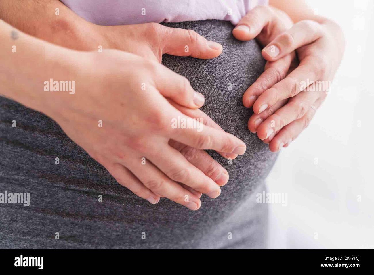 a Close-up of a male and female hands holding on a pregnant woman's belly - a hypnobirthing concept Stock Photo
