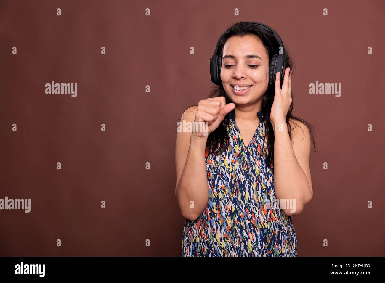 Smiling indian woman in headphones, singing in imaginable microphone, listening to music with