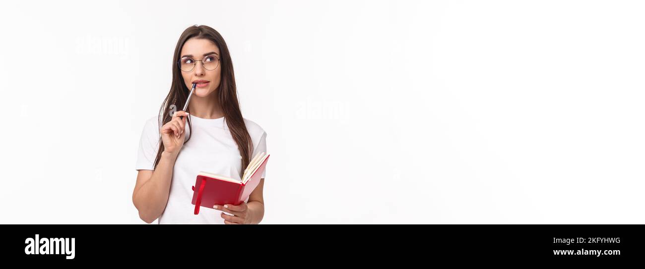 Portrait of creative and thoughtful gorgeous young woman making plans for next weekend in her planner, biting pen pondering what write in notebook Stock Photo